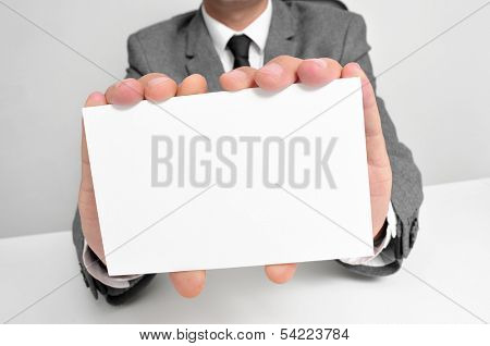 a man wearing a suit sitting in a desk holding a blank signboard with a copy-space