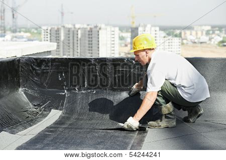 Roofer preparing part of bitumen roofing felt roll for melting by gas heater torch flame