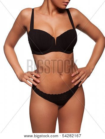 Close up view of the shapely curvaceous body of a sexy tanned young woman in black lingerie standing with her hands to her hips, torso view on white