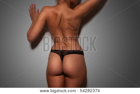 Close up view of the shapely curvaceous body of a sexy tanned young woman in black lingerie standing with her hands to her hips, torso view on white