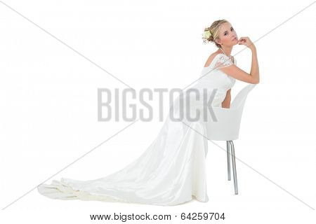 Side view portrait of confident bride with hand on chin leaning on chair over white background
