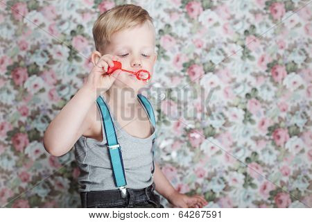 Beautiful joyful blond boy blowing soap bubbles