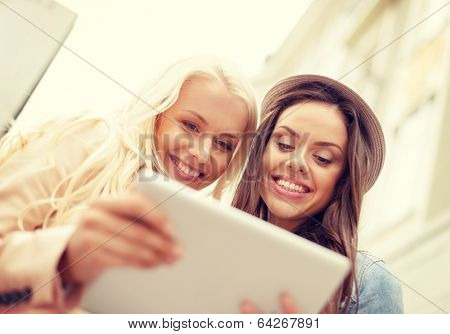 holidays, technology and tourism concept - two beautiful girls toursits looking into tablet pc in the city