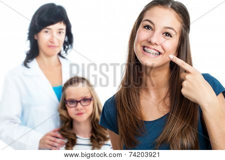 Teen Girl Pointing At Dental Barces With Doctor In Background.