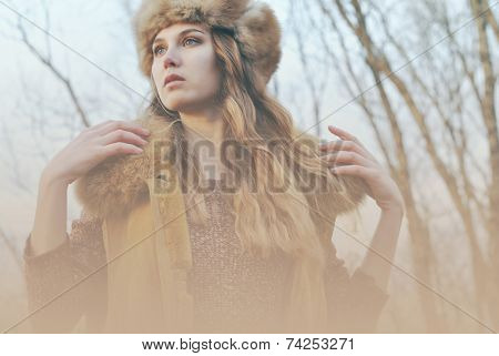 Girl in fur coat posing at branches background