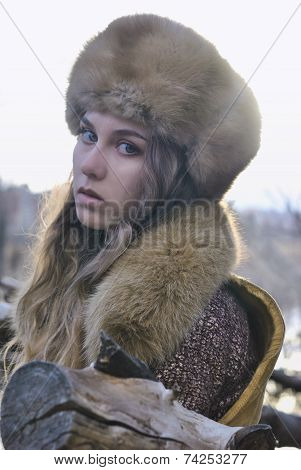 portrait photo of blond hair wind girl looking to camera wearing fur hat in early spring