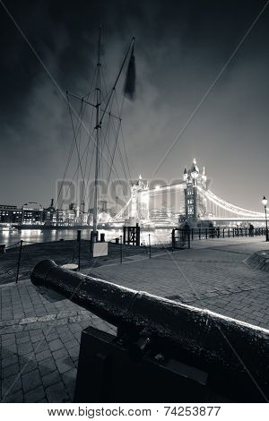 Cannon and Tower Bridge at night at St. Katherine Dock in London.