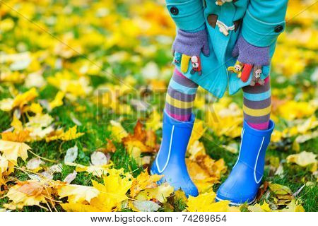 Close up of a little girl in colorful clothes and blue boots outdoors at beautiful autumn park