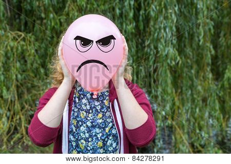 Girl holding balloon with angry face outdoors