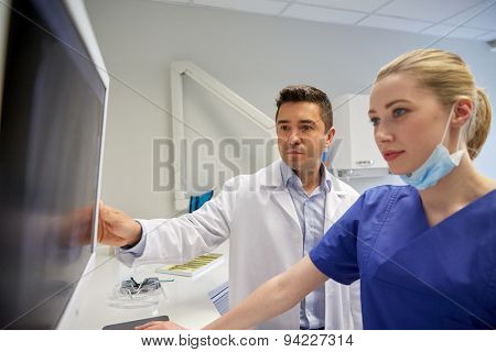 people, medicine, stomatology, technology and health care concept - dentists looking to x-ray scan on monitor at dental clinic