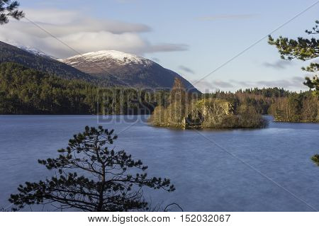 View over Loch an Eilein showing its island with a castle ruin and snow-covered mountain in the background
