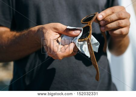 Unrecognizable man polishing lens of elegance wooden sunglasses with soft napkin