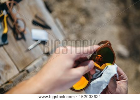 Reflection in lens of bearded man polishing sunglasses with soft napkin. Tools at background