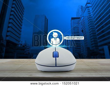 Wireless computer mouse with businessman and magnifying glass icon on wooden table over city tower Recruitment concept