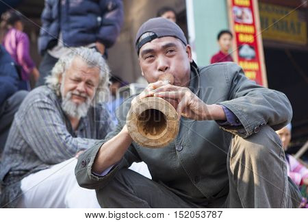 Bac Ha, Vietnam - Oct 17, 2015: Vietnamese civilian artist performing traditional melody with a wooden trumpet at a weekly flea market. Bac Ha along with Sapa are well known favorite destination.