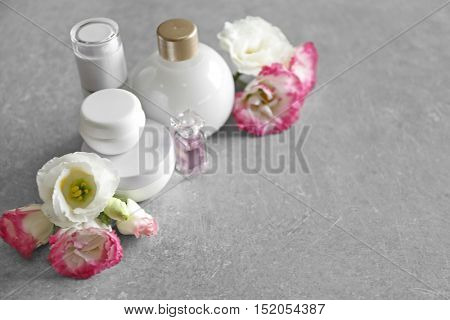 Cosmetic bottles and eustoma flowers on light wooden background