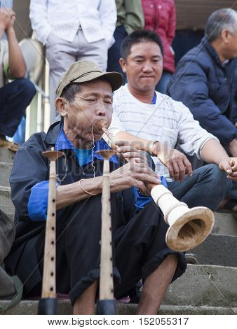 Bac Ha, Vietnam - Oct 17, 2015: Vietnamese civilian artist performing traditional melody with a wooden trumpet at a weekly flea market. Bac Ha along with Sapa are well known favorite destination.