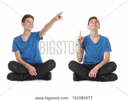 Cute teenager boy poinitng up side in blue T-shirt and lotus posture over white isolated background