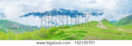 The green valley in Kazbegi National Park leads to the Gergeti Trinity Church with the heavy clouds on the background Georgia.