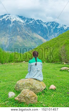 The girl sits on the boulder in the middle of the green forest glade in Kazbegi National Park Georgia.
