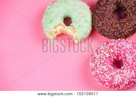 Sweet colorful tasty donuts with icing and sprinkles on pastel pink background.