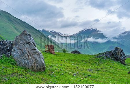 The stone heads of the famous poets and writers on the green meadow in misty gorge of Sno village Georgia.