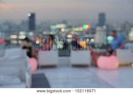 blur photo of people at  luxury rooftop bar drinking and hangout with background view of bokeh city light - evening twilight time