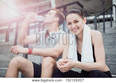 Before a good run. Happy delighted young friends waiting for their training and sitting on a stadium stairs while enjoying a sunny day together.