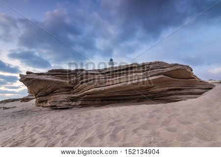 Large sandstone rock on the beach of Cape Trafalgar. With the Trafalgar lighthouse jutting. Costa de la Luz Cadiz Spain.