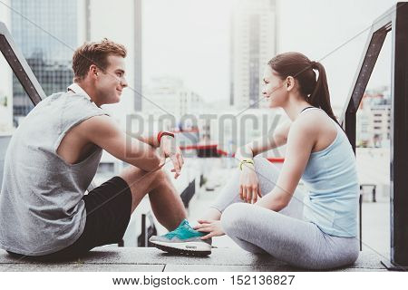 Cheerful relaxation. Beautiful slim woman and a handsome man smiling and looking at each other after working out in an urban setting.