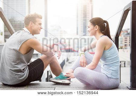 Pleasant relaxation. Beautiful young woman and a handsome fit man smiling at each other and relaxing after working out in an urban environment.