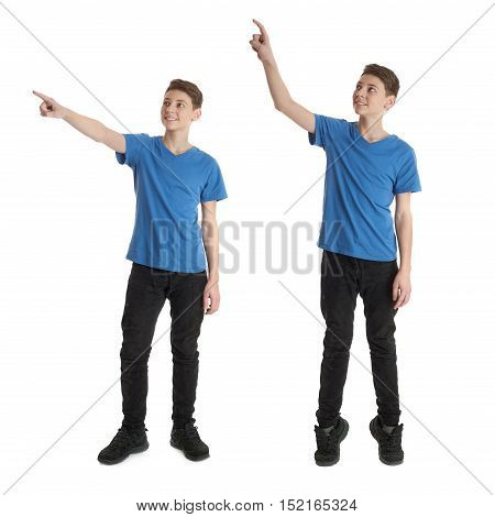 Cute teenager boy in blue T-shirt standing and poinitng up side over white isolated background full body