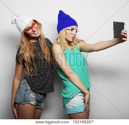 two hipster girls friends taking selfie with digital tablet, studio shot over gray vackground