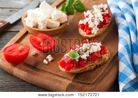 Bruschetta with tomatoes feta cheese and basil. Traditional Greek snack on wooden background. Selective focus.