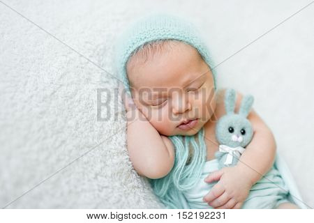 lovely sleeping baby with blue hat, panties and toy on white blanket close up