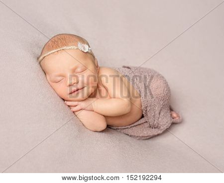 smiling sleeping newborn girl with hands under her head covered with knitted shawl
