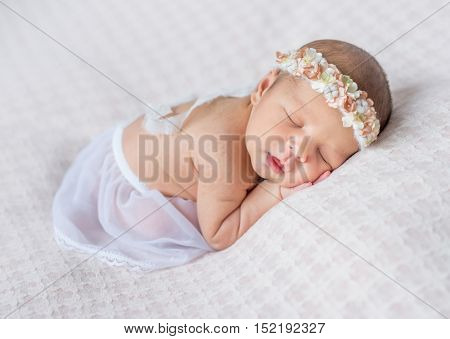 lovely newborn girl with headband sleeping on her stomach and hands under her head, covered with white shawl