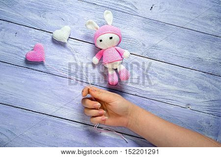 girls hand holding balloons crocheted giving the hearts to knit bunny as a birthday gift. wooden background with copy space for your congratulatory text