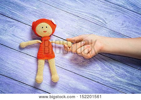 Crocheted Doll Girl And This Girl's Hand On The Wooden Background With Free Place For Your Inscripti