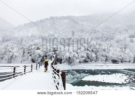 People crossing the bridge over Shogawa river at historic Japanese village Shirakawa-go at winter, one of Japan's UNESCO world heritage sites