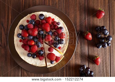 Close up. Delicious Homemade creamy New York Cheesecake with berries on dark wooden table. Top viev. Cream mousse cake.