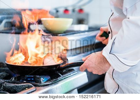 Chef doing flambe to dish in pan with large fire flame
