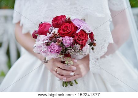 Beautiful bride is holding a wedding colorful bouquet. Beauty of colored flowers. Close-up bunch of florets. Bridal accessories. Female decoration for girl. Details for marriage and for married couple