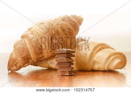 Two baked croissants with chocolate bars. on a wooden surface. White background
