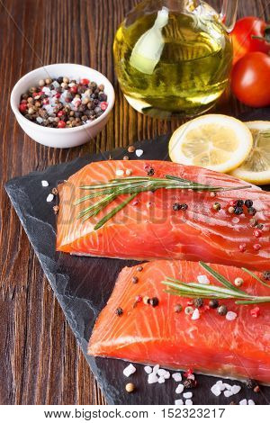 Raw salmon fillet and ingredients for cooking on a slade board and brown wooden background.