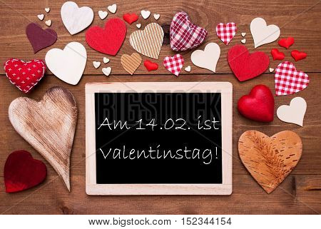 Chalkboard With German Text Valentinstag Means Valentines Day. Many Red Textile Hearts. Wooden Background With Vintage, Rustic Or Retro Style.