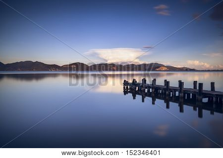 Wooden pier or jetty on blue lake sunset and sky reflection water. Long exposure Versilia Massaciuccoli Tuscany Italy.