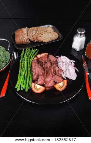 business lunch fresh roast beef meat slices on black plate wotj cutlery asparagus boiled broccoli rye bun on wooden table