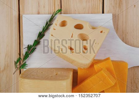 various types of fresh raw aged delicatessen cheese on white plate over light wooden table cheddar edam swiss