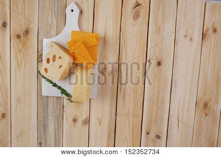various types of fresh raw aged delicatessen cheese on white plate over light wooden table cheddar edam swiss